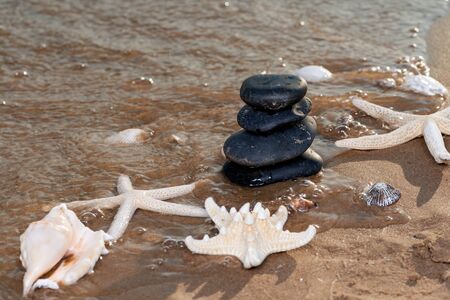 Spa composition - stacked Basalt Stones, Seashells and Sea Stars on the beach at sunrise in front of the ocean. Wellness, Balance and Relax concept.の写真素材