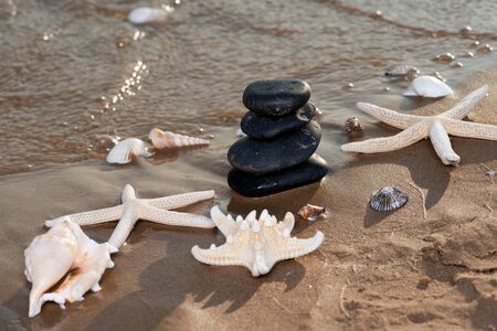 Spa composition - stacked Basalt Stones, Seashells and Sea Stars on the beach at sunrise in front of the ocean. Wellness, Balance and Relax concept.の写真素材