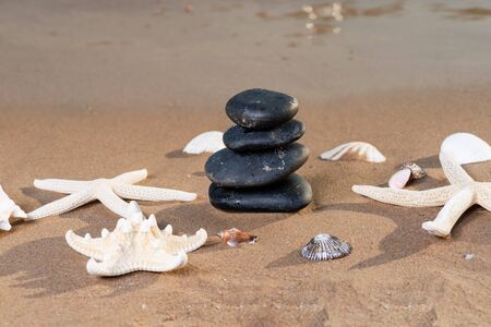 Spa composition - stacked Basalt Stones, Seashells and Sea Stars on the beach at sunrise in front of the ocean. Wellness, Balance and Relax concept.の写真素材