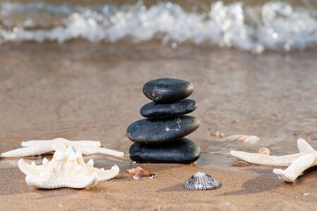 Spa composition - stacked Basalt Stones, Seashells and Sea Stars on the beach at sunrise in front of the ocean. Wellness, Balance and Relax concept.の写真素材