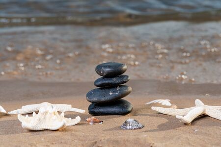 Spa composition - stacked Basalt Stones, Seashells and Sea Stars on the beach at sunrise in front of the ocean. Wellness, Balance and Relax concept.の写真素材