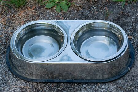 Stainless steel Bowls with Fresh Water for Thirsty Dogs put outdoors on the sidewalk where people...