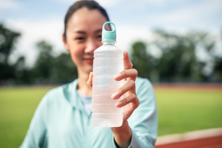 Focus drinking water bottle. Athletic young asian woman holding drinking water bottle and show to...
