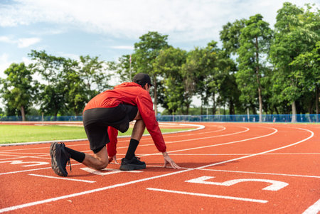 Young Asian man runner using starting block to start his run on running track background, outdoor...