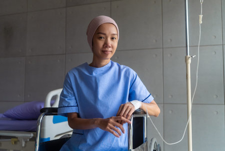 Asian woman cancer patient sitting alone in wheelchair looking outside window in hospital ward with...