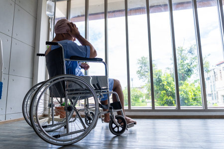 Asian man cancer patient sitting alone in wheelchair looking outside window in hospital ward with...