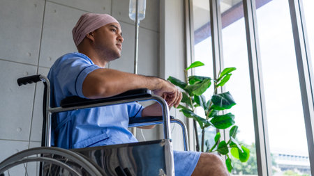 Asian man cancer patient sitting alone in wheelchair looking outside window in hospital ward with...
