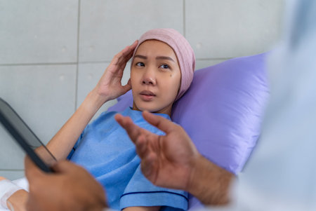 Asian woman patient describes her symptoms to an oncologist while sitting on a bed and looking at a...