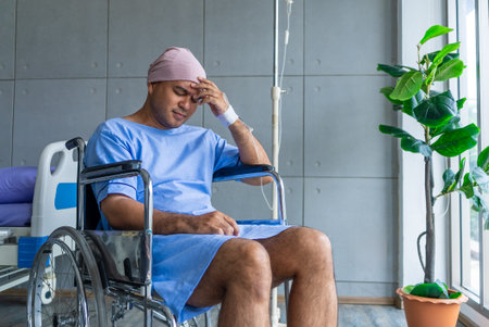 Asian man cancer patient sitting alone in wheelchair looking outside window in hospital ward with...