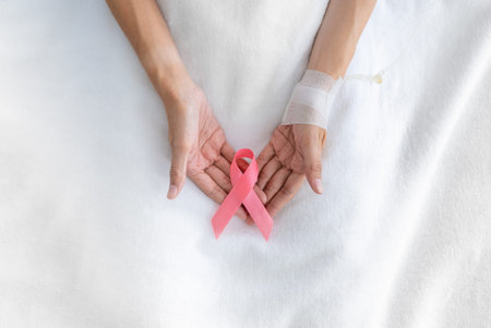 Close up of asian woman breast cancer patient placing pink ribbon on hand as symbol of breast cancer awareness. Breast cancer awareness concept.の写真素材