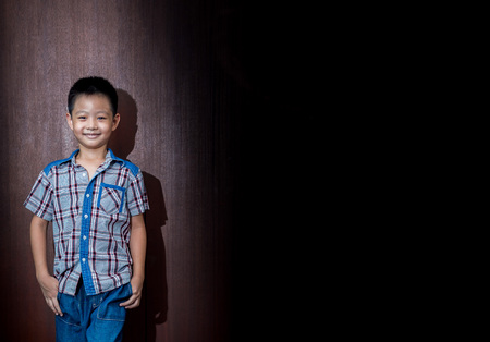 little cute boy on wood background gesture smiling closeup, hand in the pocketsの写真素材