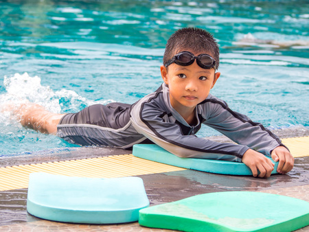Asian boy swimming with the board in the pool