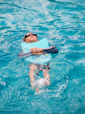 Asian boy swimming with the board in the poolの写真素材