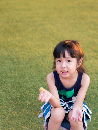 Happy kid, asian baby child eating a  cookie on the lawnの写真素材