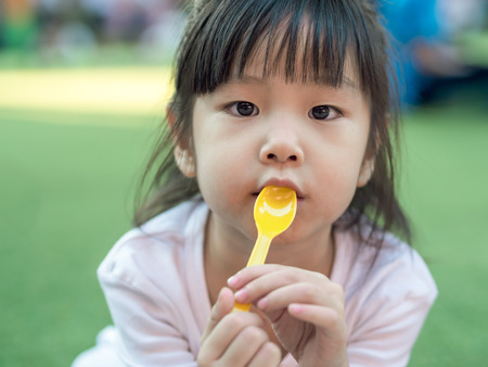 Asian girl child eating a dessert , spoon in her mouthの写真素材