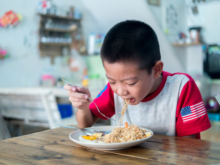 Happy Asian boy eating delicious noodleの写真素材
