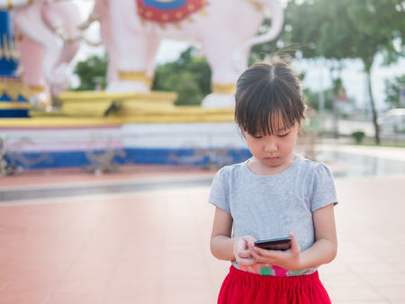 Asian child girl play smart phone, in the gardenの写真素材