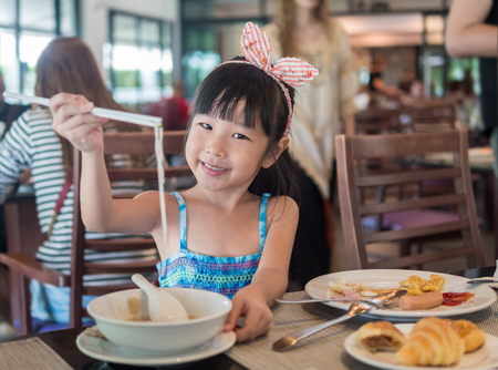 Happy Asian child eating delicious noodle with chopstick, in the restaurantの写真素材