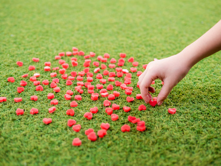 one small hand pick try to pick the heart shape made from candle on artificial grass, selective focusの写真素材