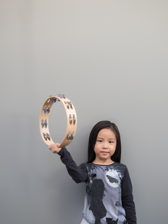 Little asian child play the tambourine, gray backgroundの写真素材