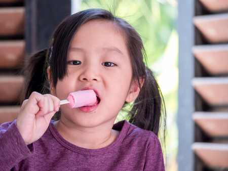 Little Asian girl eating ice cream, wood shade stripes backgroundの写真素材