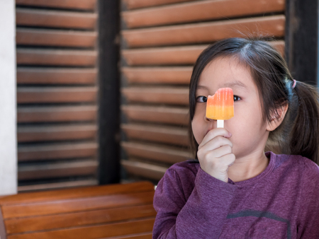 Little Asian girl eating ice cream, wood shade stripes backgroundの写真素材