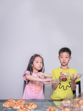 Adorable kid girl and boy separate packing baked pork sausage with mayonnaise bread,  domestic kitchen, Child  helping his parentsの写真素材