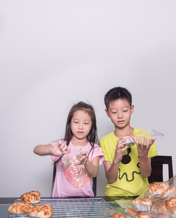 Adorable kid girl and boy separate packing baked pork sausage with mayonnaise bread,  domestic kitchen, Child  helping his parentsの写真素材