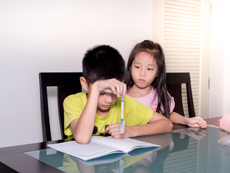 Asia little sister look her brother studying and doing his homework  at home,  on the table, home education, thinking actionの写真素材