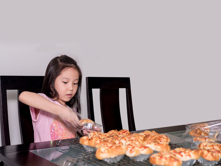 Adorable  kid girl separate packing baked pork sausage with mayonnaise bread,  domestic kitchen, Child  helping his parentsの写真素材