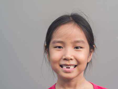 Asian little cute girl smile with her broken tooth , grey background