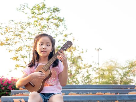 Little asian child girl play the ukulele, in the garden on the Steel pipeの写真素材