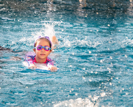 Asian child or kid girl wearing swimming suit to learning on swimming pool , learn and training swim on kick boardの写真素材