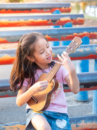 Little asian child girl play the ukulele, in the garden on the Steel pipe, practice to playの写真素材