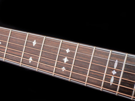 The neck of a six-string acoustic guitar on a dark background . guitar neck on a black background....