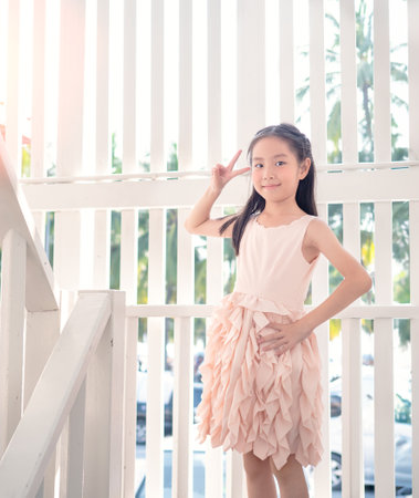 Asia girl smiling looking to the camera showing fingers doing victory sign. Number two.white fence backgroundの写真素材