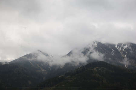 foggy clouds rising from dark alpine mountain forestの写真素材