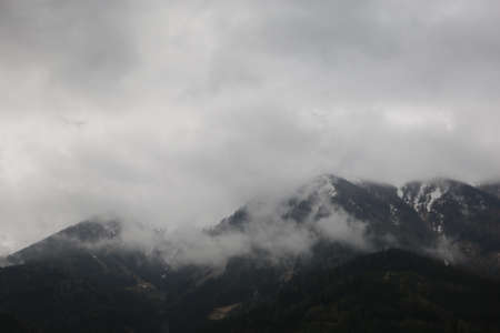 foggy clouds rising from dark alpine mountain forestの写真素材