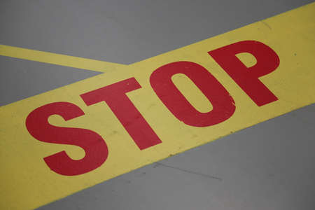 Stop sign written in red letters with yellow line on gray groundの写真素材