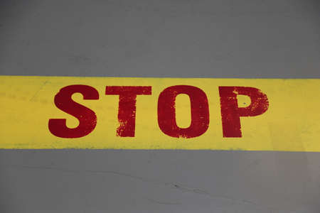 Stop sign written in red letters with yellow line on gray groundの写真素材