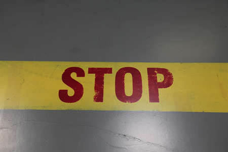 Stop sign written in red letters with yellow line on gray groundの写真素材