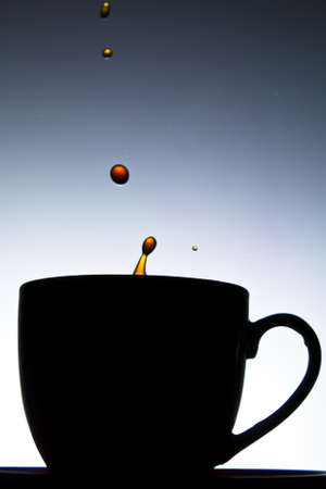 Coffee splashing into cup in silhouetteの写真素材