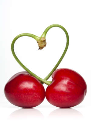 Pair of cherries against a white backdrop with the stems forming a heart symbolの写真素材