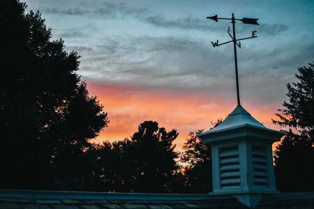 A Colorful Sunset With Trees Over a Roof Topの写真素材
