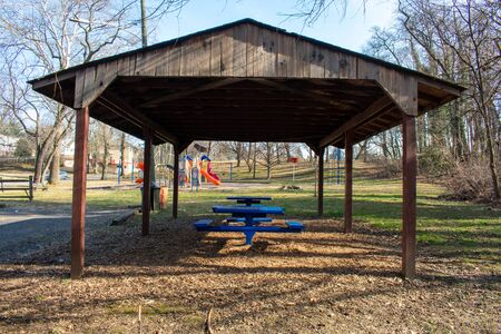 A Wooden Gazebo in a Park With Blue Benches Under it and a Playground in the backgroundの写真素材