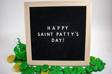 A Black Sign With White Letters That Says Happy Saint Patty's Day on a White Background With Glitter Clovers and Gold Coins Around Itの写真素材