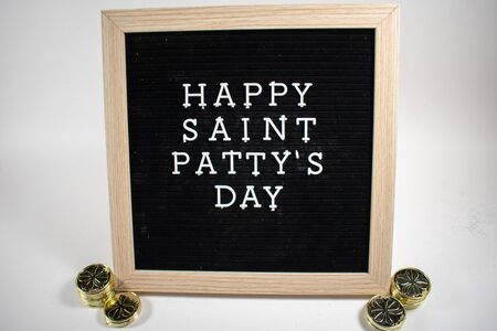 A Black Sign With White Letters That Says Happy Saint Patty's Day on a White Background With Gold Coinsの写真素材