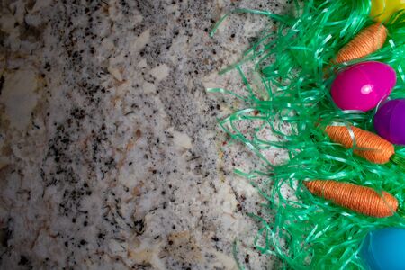 An Easter Flat Lay With Easter Grass, Carrots, and Eggs on a Granite Counter Top With Copy Space