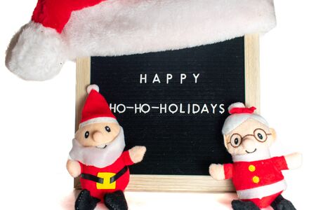 A Black Sign With White Letters in a Birch Frame That Says Happy Holidays With Santa Claus, Mrs. Claus, and a Christmas Hat on Top.の写真素材