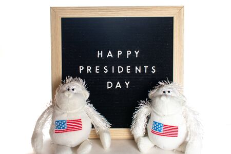A Black Sign With White Letters That Says Happy Presidents Day With Two White Stuffed American Flag Monkeys in Front of it.の写真素材